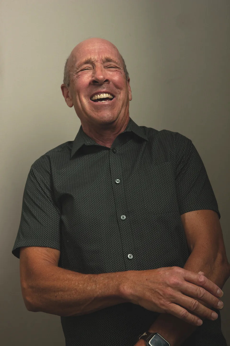 Jeff Allen laughing with arms folded, in a dark short-sleeve shirt against a gray backdrop
